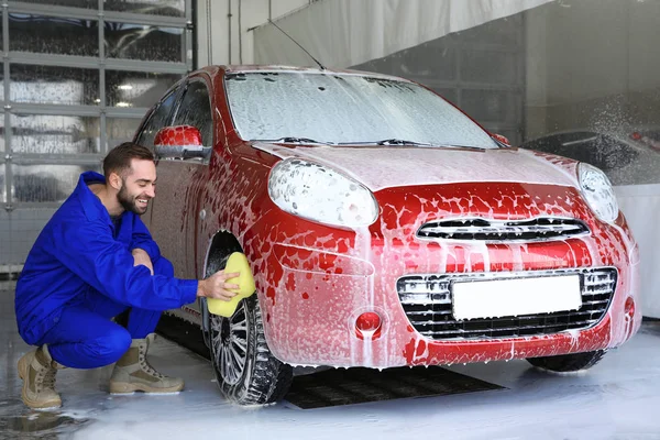 Young worker cleaning automobile wheel at car wash — Stock Photo, Image