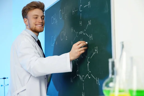 Cientista masculino escrevendo fórmula química em chalkboard dentro de casa — Fotografia de Stock