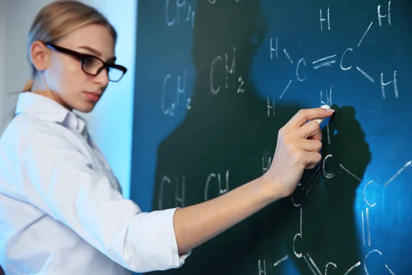 Cientista feminina escrevendo fórmula química em quadro-negro dentro de casa — Fotografia de Stock
