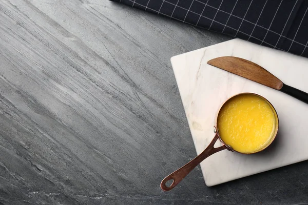 Tablero de piedra con cacerola de mantequilla clarificada y cuchillo sobre mesa, aplanado. Espacio para texto — Foto de Stock