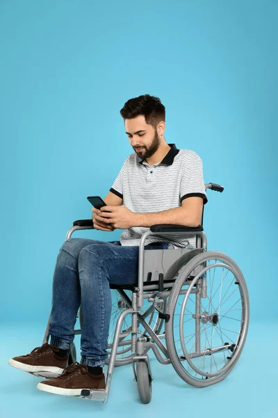 Junger Mann mit Smartphone im Rollstuhl auf farbigem Hintergrund — Stockfoto