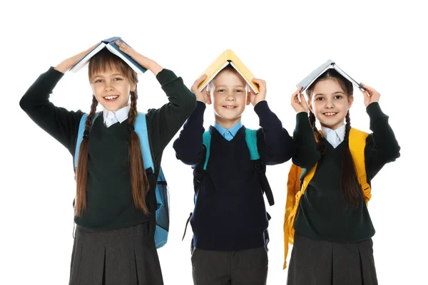 Portrait d'enfants drôles en uniforme scolaire avec des livres sur les têtes sur fond blanc — Photo