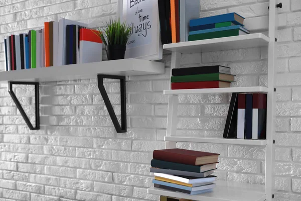 Scaffali con diversi libri su muro di mattoni bianchi — Foto Stock