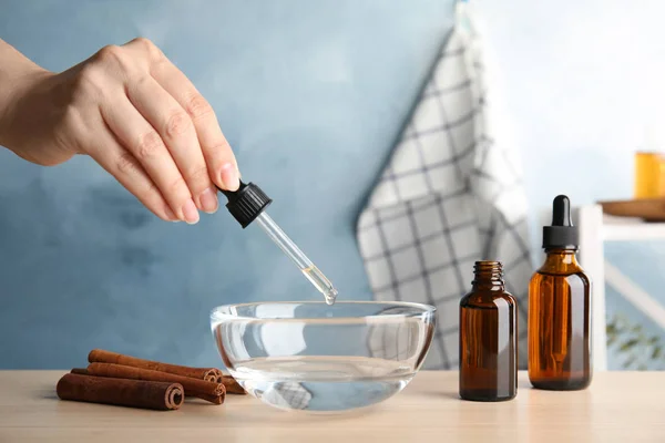 Mujer goteando aceite esencial de canela de la pipeta en un tazón de agua en la mesa, primer plano — Foto de Stock