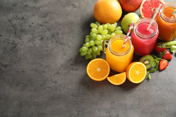 Verschiedene Säfte in Einmachgläsern und frisches Obst auf einem grauen Tisch. Raum für Text — Stockfoto