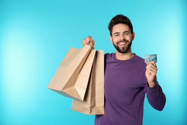 Portrait de jeune homme heureux avec carte de crédit et sacs à provisions sur fond de couleur, espace pour le texte. Dépense d'argent — Photo