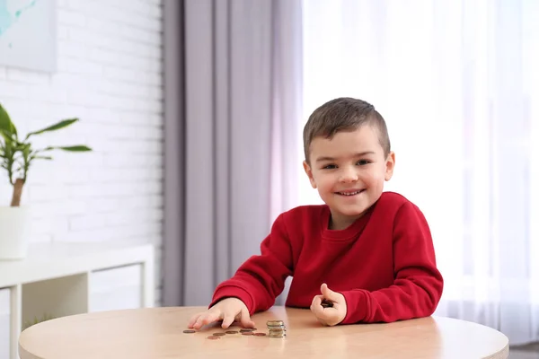 Lindo niño pequeño con monedas en casa. Contando dinero —  Fotos de Stock