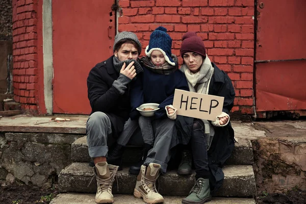 Povera giovane famiglia con HELP segno su strada sporca — Foto Stock