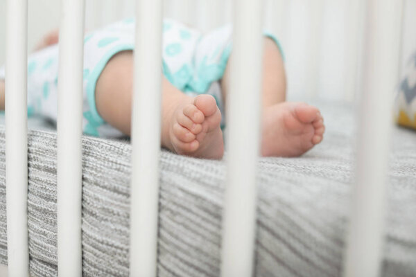 Little baby lying in crib, closeup of legs