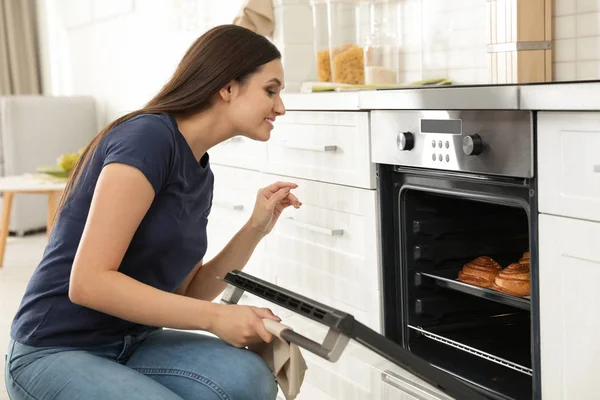 Mulher bonita que abre a porta do forno com pães cozidos na cozinha — Fotografia de Stock
