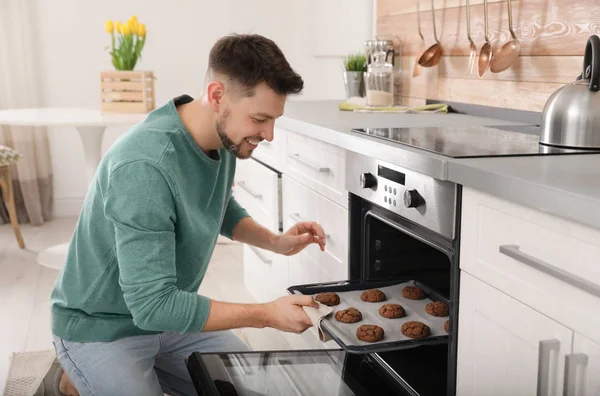 Homem bonito tirando bandeja de biscoitos cozidos do forno na cozinha — Fotografia de Stock