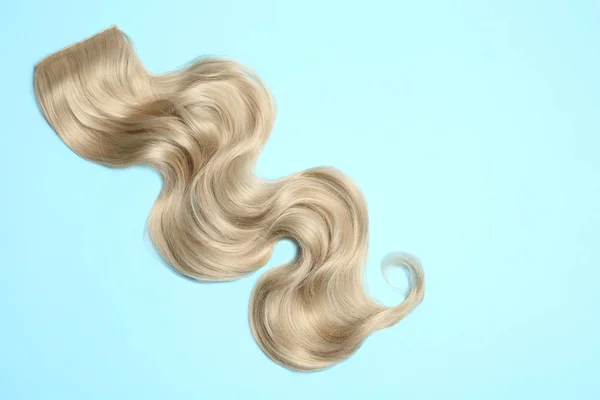 Lock of blonde wavy hair on color background, top view. Space for text — Stock Photo, Image