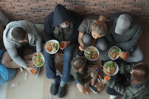 Arme mensen met borden van voedsel zittend aan de muur binnenshuis, uitzicht vanaf boven — Stockfoto