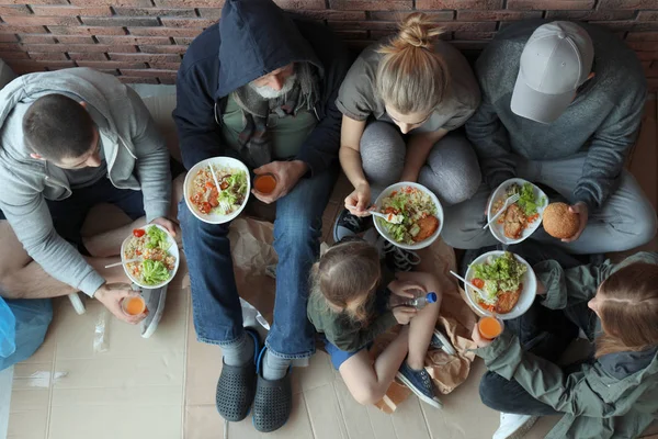 Pobres personas con platos de comida sentados en la pared en el interior, vista desde arriba — Foto de Stock
