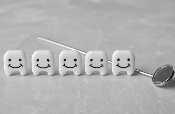 Dekorativa tänder och tandläkare spegel på grått bord, närbild — Stockfoto