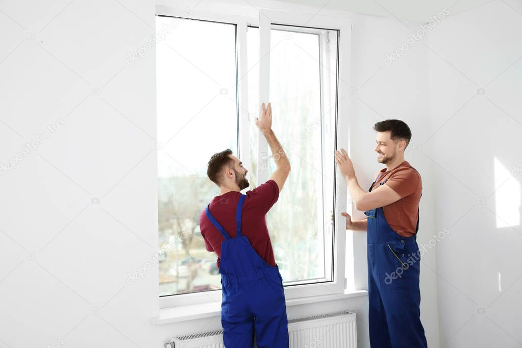 Construction workers installing plastic window in house