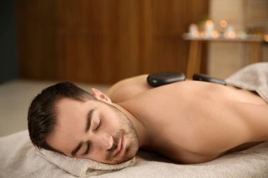 Yakışıklı adam spa salonunda sıcak taş masajı alıyor. Metin için alan