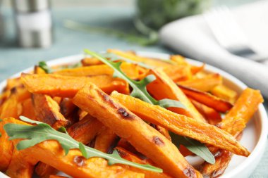 Tabak pişmiş tatlı patates dilimleri ve masada arugula ile, closeup