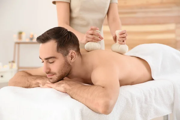 Hombre guapo recibiendo masaje bolsa de hierbas en el salón de spa —  Fotos de Stock
