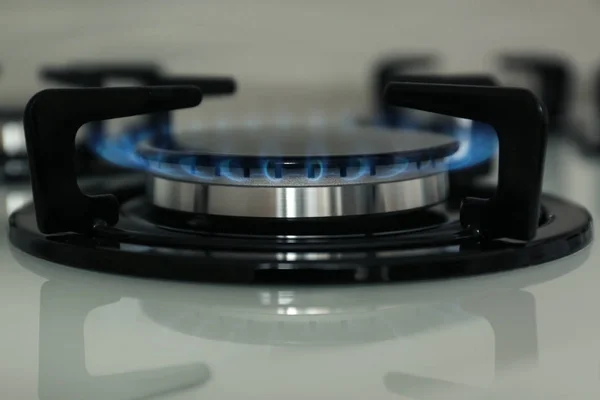 Gas burner with blue flame on modern stove, closeup