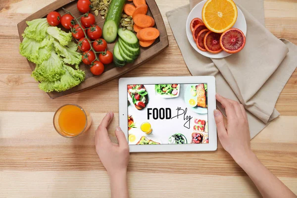 Food blogger with tablet computer, fresh fruits and vegetables on wooden background, top view