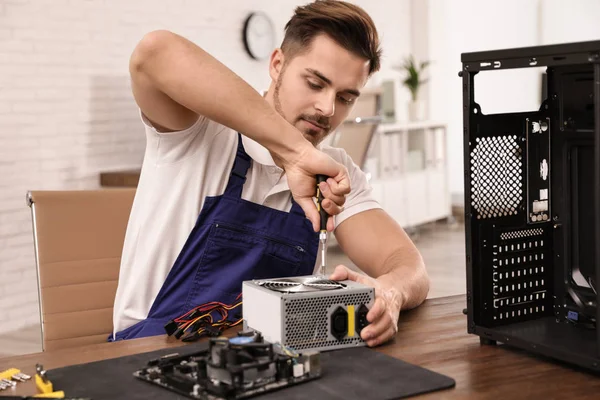 Male technician repairing power supply unit at table indoors — Stock Photo, Image