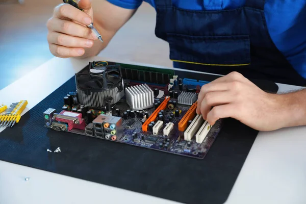 Male technician repairing motherboard at table, closeup