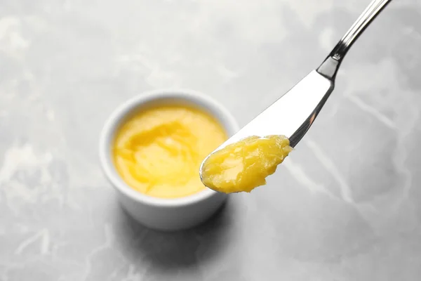 Cuchillo con mantequilla clarificada sobre mesa gris — Foto de Stock