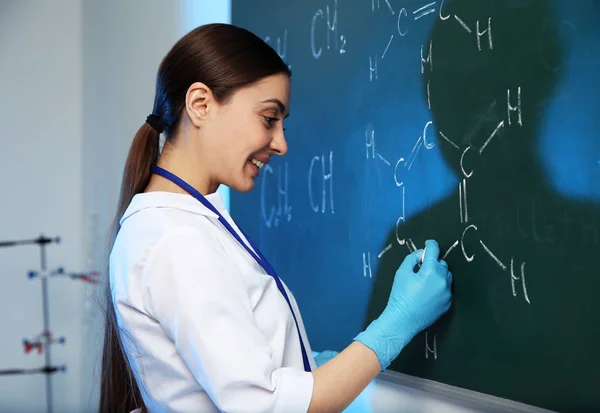 Cientista feminina escrevendo fórmula química em quadro-negro dentro de casa — Fotografia de Stock
