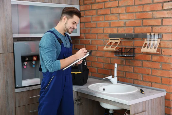 Plomero masculino con portapapeles cerca del fregadero de la cocina. Servicio de reparación — Foto de Stock