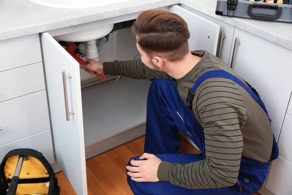 Мужчина-сантехник в форме, ремонтирует кухонную раковину — стоковое фото