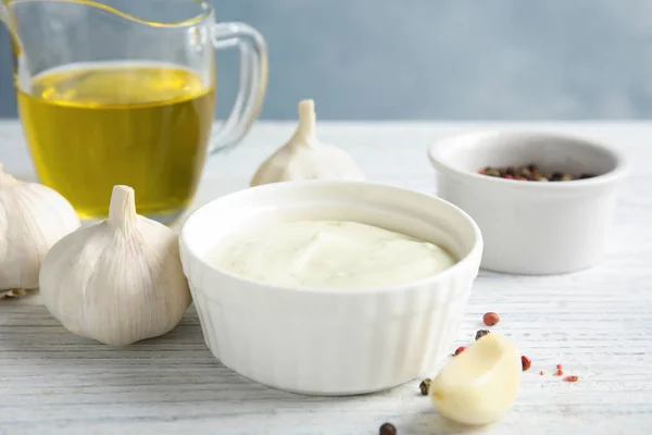 Verse knoflook en kom van saus op witte houten tafel — Stockfoto