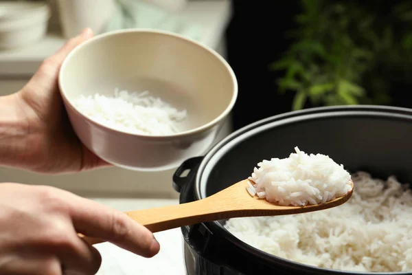 Woman putting tasty rice into bowl from cooker in kitchen, closeup — Stock Photo, Image