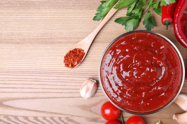 Kom met hete chili saus en ingrediënten op houten achtergrond, platte lay. Ruimte voor tekst — Stockfoto