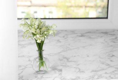 Beautiful lily of the valley bouquet in vase on windowsill, space for text
