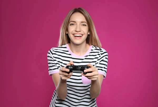 Emotional young woman playing video games with controller on color background — Stock Photo, Image