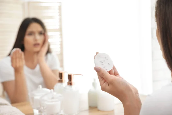 Mulher bonita segurando almofada de algodão com pestanas caídas perto do espelho dentro de casa, close-up — Fotografia de Stock