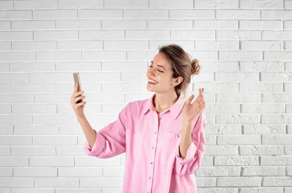 Mujer usando el teléfono móvil para el chat de vídeo contra la pared de ladrillo — Foto de Stock
