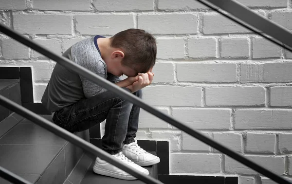 Triste menino sentado nas escadas dentro de casa — Fotografia de Stock