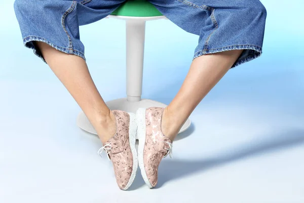 Woman in stylish shoes on stool against color background, closeup