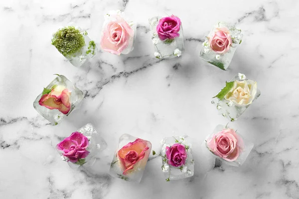 Frame made of ice cubes with flowers on marble background, flat lay. Space for text