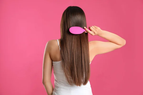 Back view of young woman with hair brush on color background — Stock Photo, Image