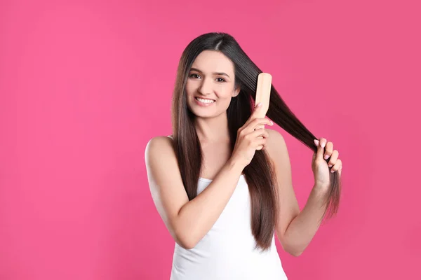 Mooie lachende jonge vrouw met haarborstel op kleur achtergrond — Stockfoto