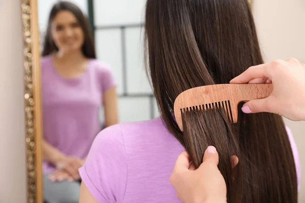 Woman combing friend\'s hair indoors, closeup view