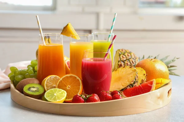 Wooden tray with glasses of different juices and fresh fruits on table — Stock Photo, Image