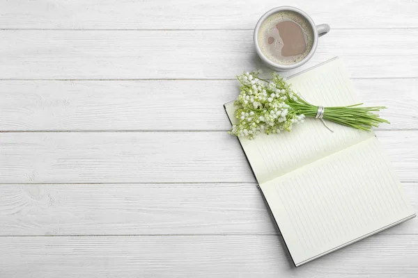 Flat lay composition with notebook, lily of the valley bouquet and coffee on white wooden background. Space for text — Stock Photo, Image