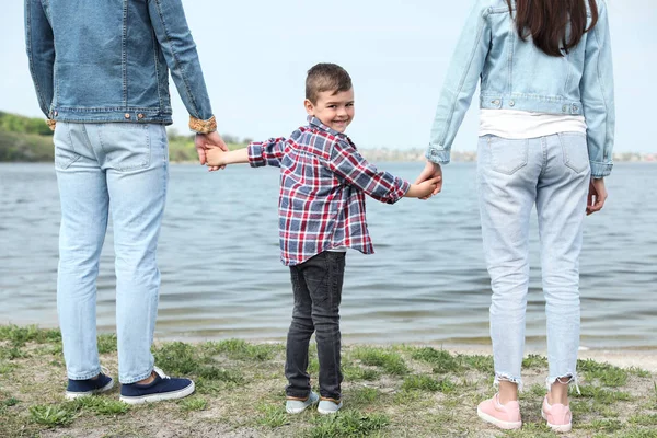 Criança pequena bonito de mãos dadas com seus pais perto do rio. Tempo de família — Fotografia de Stock