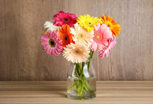 Ramo de hermosas flores de gerberas brillantes en jarrón de vidrio sobre la mesa sobre fondo de madera — Foto de Stock