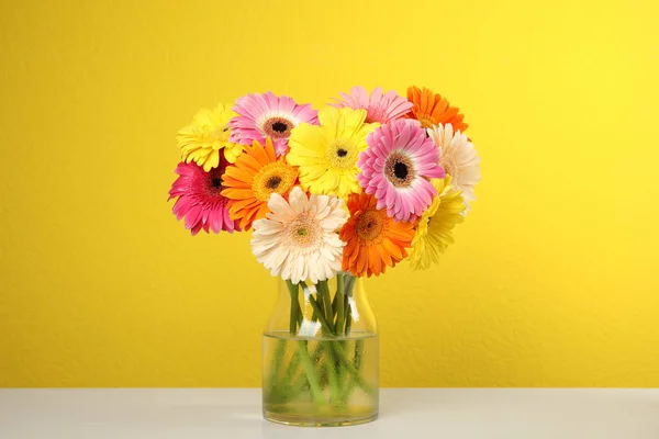 Boeket van mooie heldere Gerbera bloemen in vaas op tafel tegen kleur achtergrond — Stockfoto