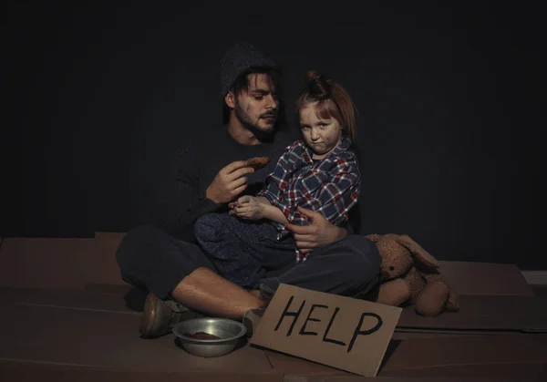 Pobre padre e hija con el cartel de AYUDA en el suelo cerca de la pared oscura — Foto de Stock